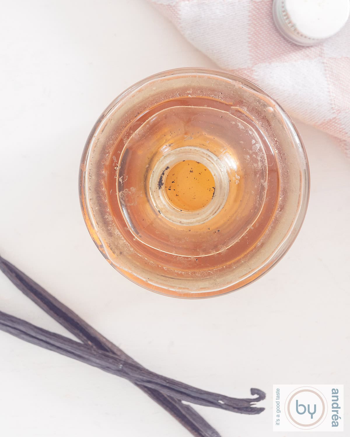 Een foto van bovenaf van een fles gevuld met vanille extract en twee vanille stokjes ernaast
