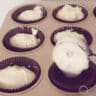 A baking tray with brown paper cases that are filled with cupcake batter with an ice cream scoop.