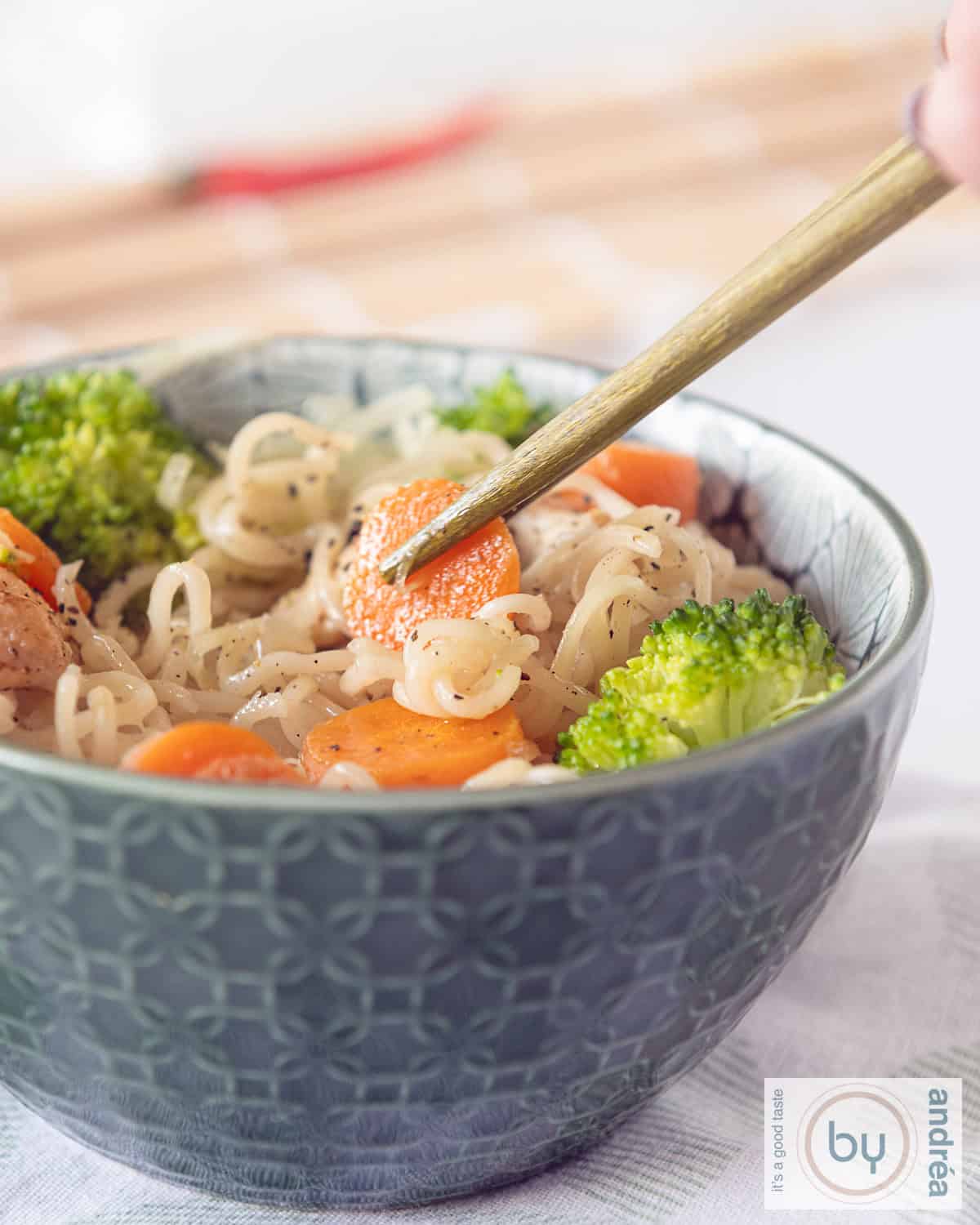 A green bowl filled with stir-fried with veggies and chicken. two chopsticks are taking a carrot