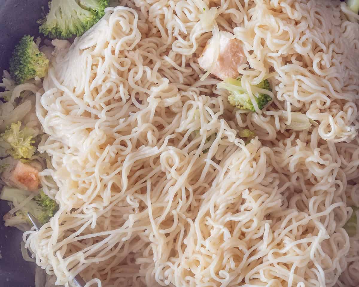 A wok filled with noodles, veggies and chicken combined.