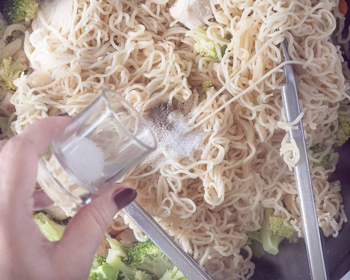 A wok filled with noodles, chicken and veggies. Sugar is added.