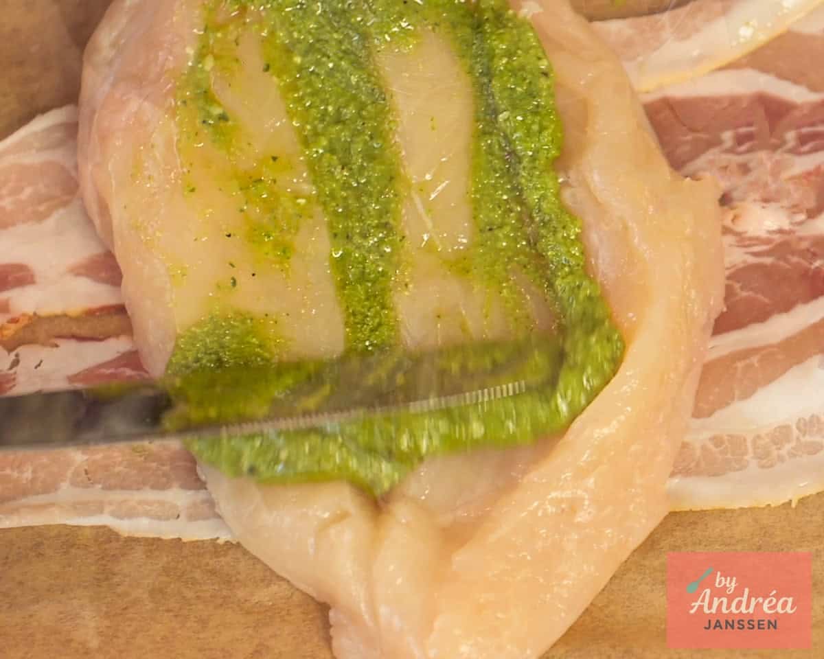 A cut open chicken fillet on which pesto is spread.