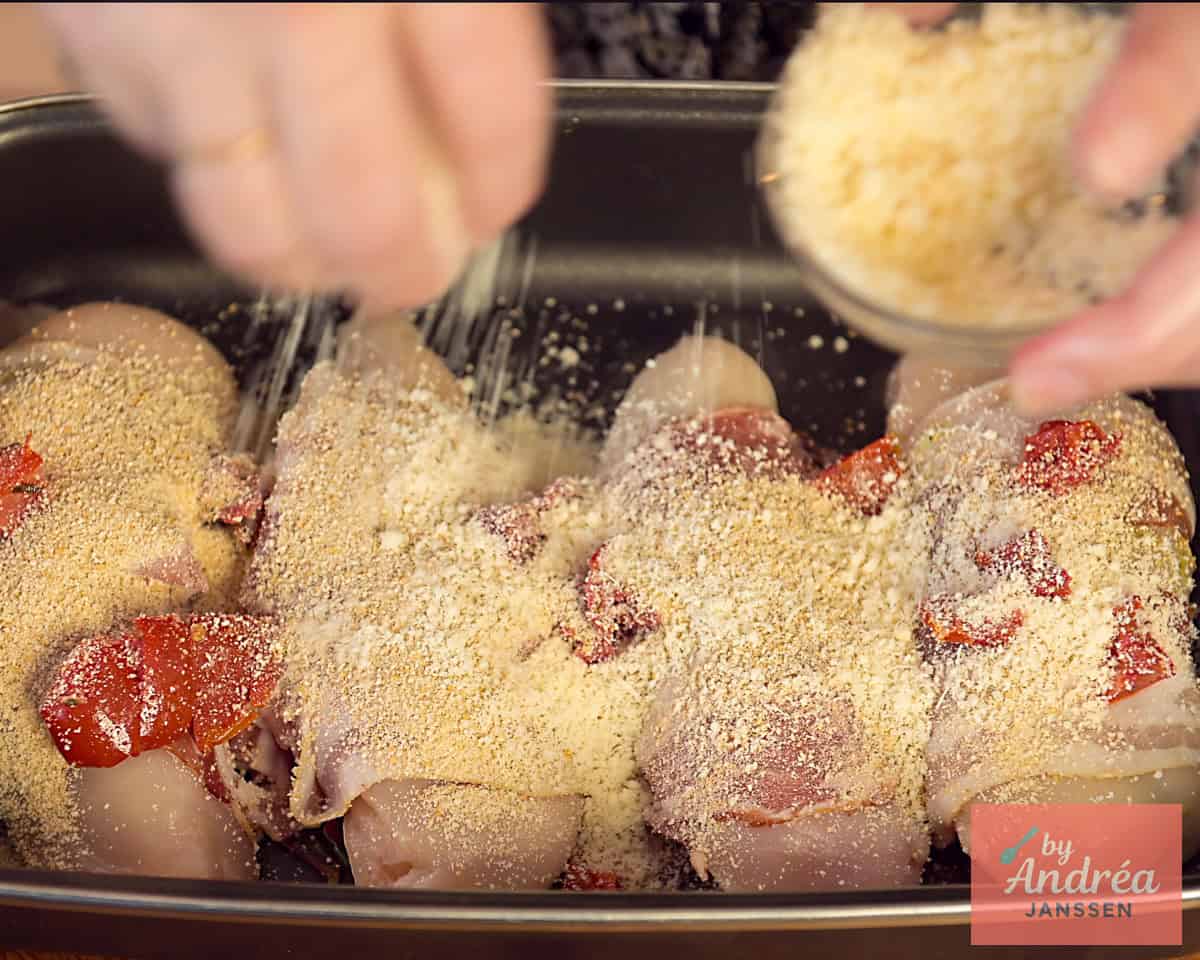 A casserole dish with stuffed chicken fillets sprinkled with sun-dried tomatoes, Parmesan cheese and breadcrumbs.