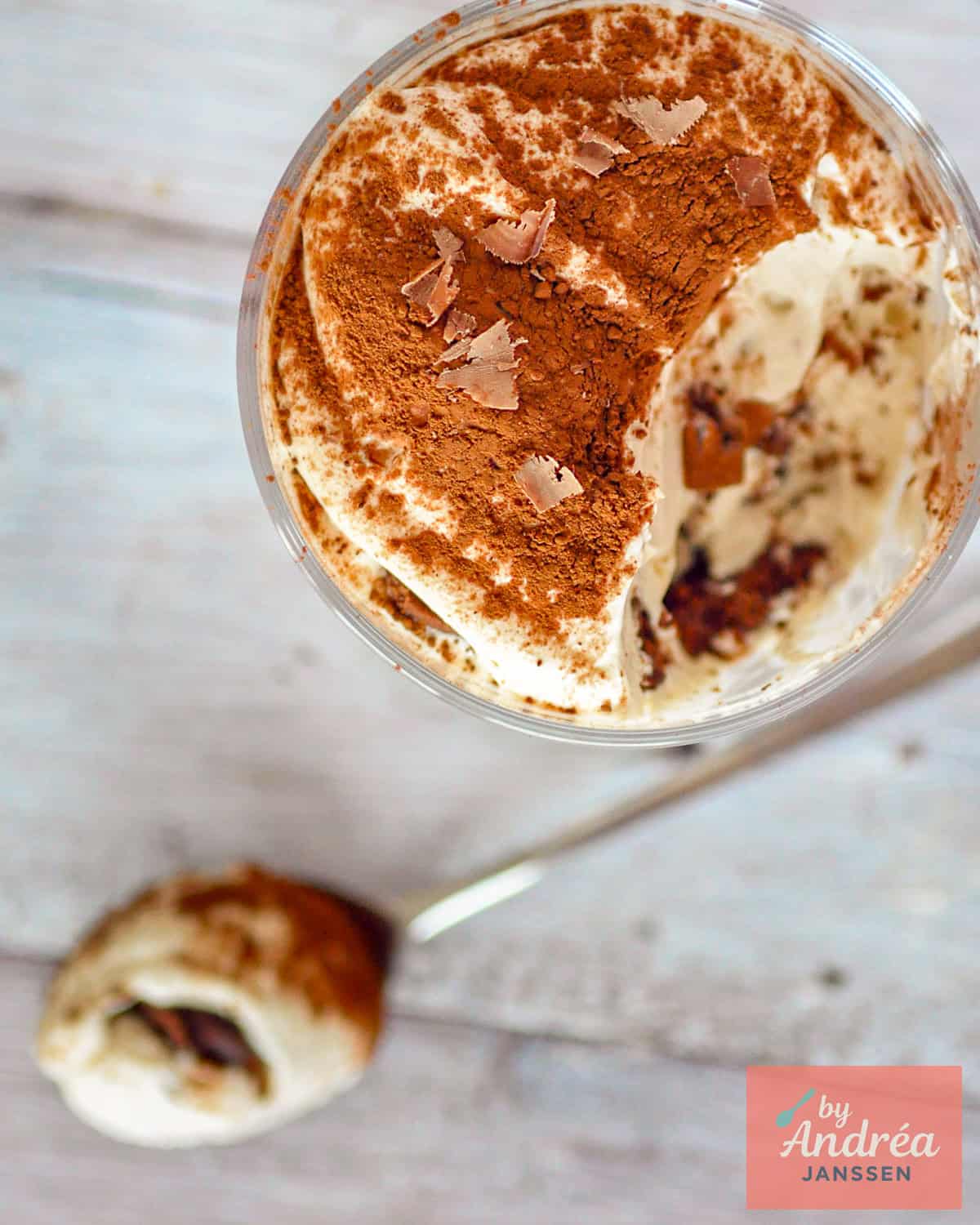 A photo from above of a glass of chocolate tiramisu on a white wooden plank surface.