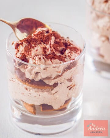 A small glass of coffee chocolate tiramisu. A spoon takes a bite.