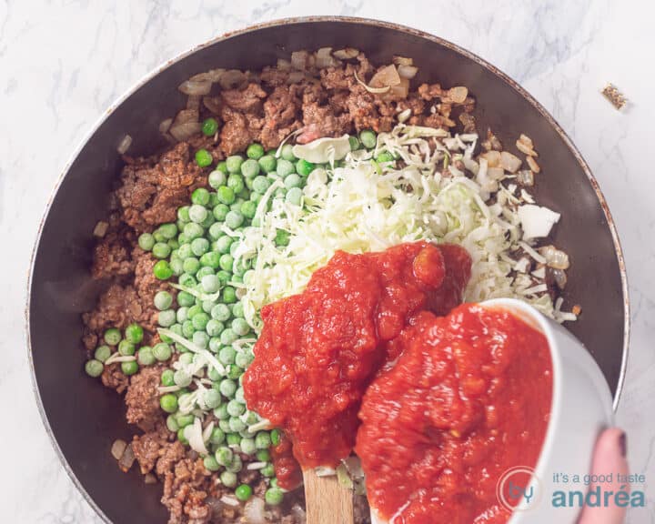 Vegetables are added to the seasoned minced meat in a frying pan.