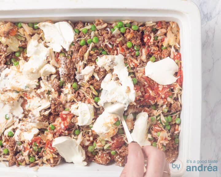 Sour cream is spread over the filling of the white baking dish