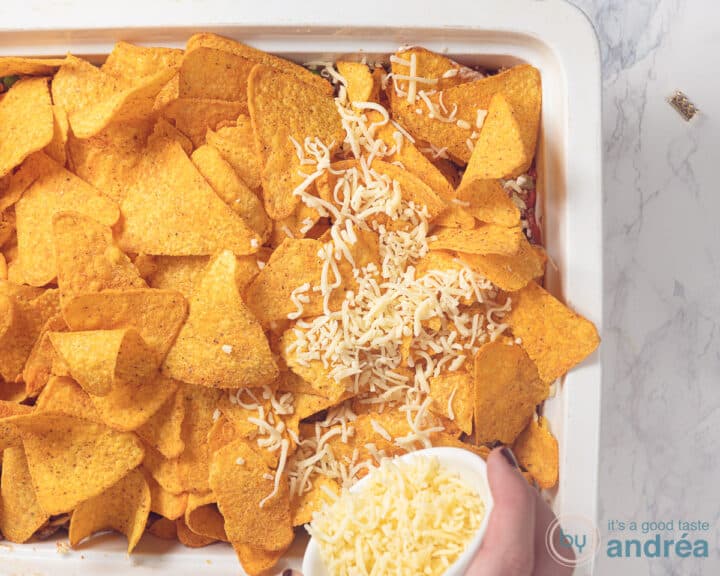 Grated cheese is sprinkled on the nachos in a white baking dish.