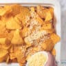 Grated cheese is sprinkled on the nachos in a white baking dish.