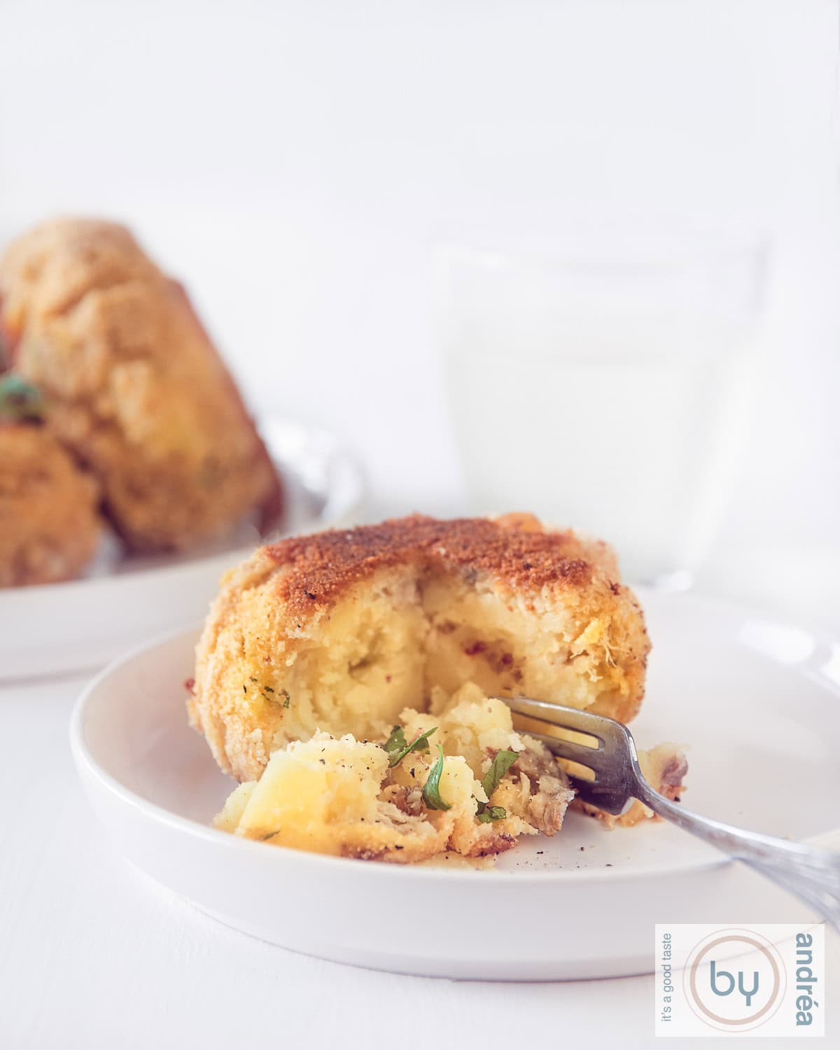 Een wit bord op een witte ondergrond met een visburger met gerookte makreel. Er is een hap uit, zodat de binnenkant goed te zien is.