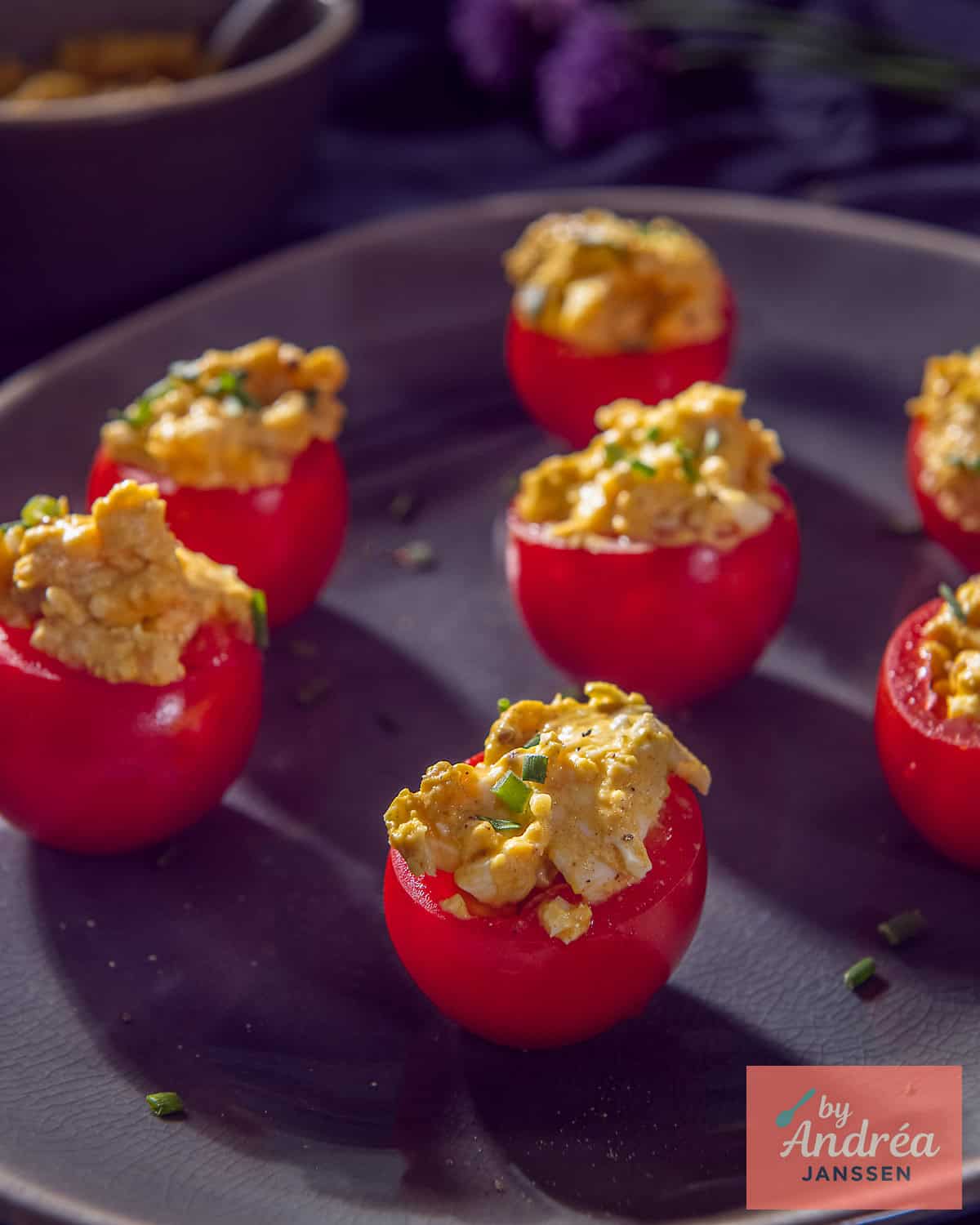 Tomatoes filled with egg salad on a grey plate.