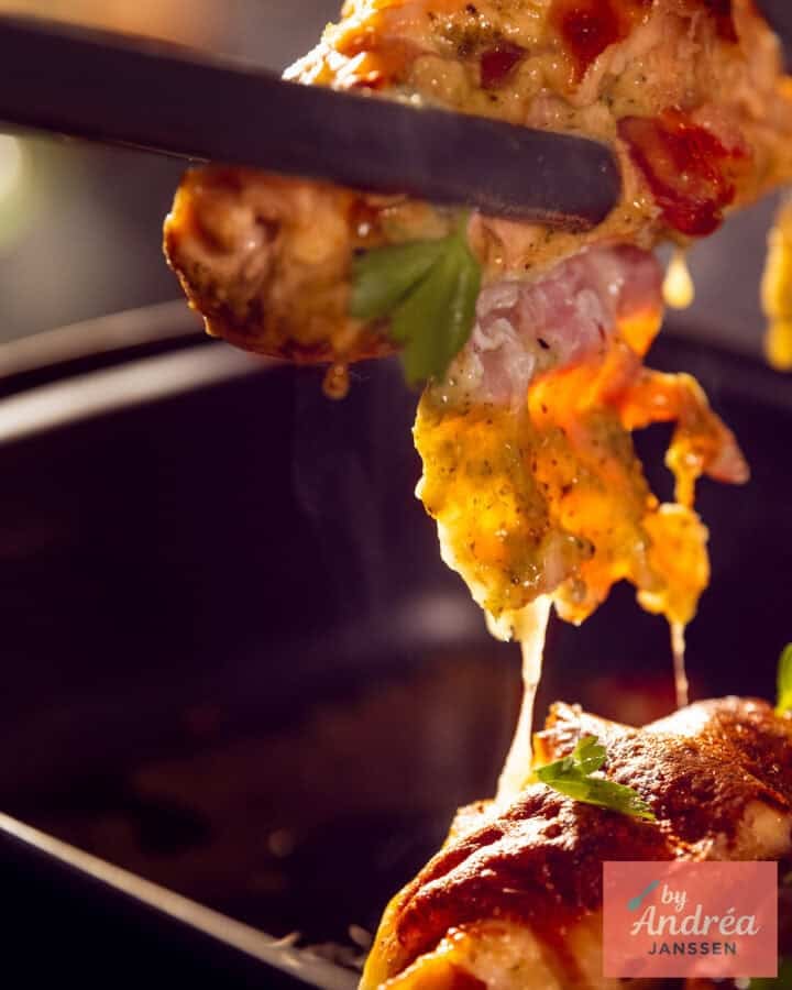 Een kipfilet die uit een ovenschaal wordt getild en de kaasdraden zijn zichtbaar!