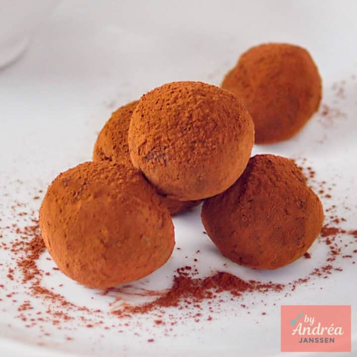 A square photo with five orange and chocolate truffles on an open white background.