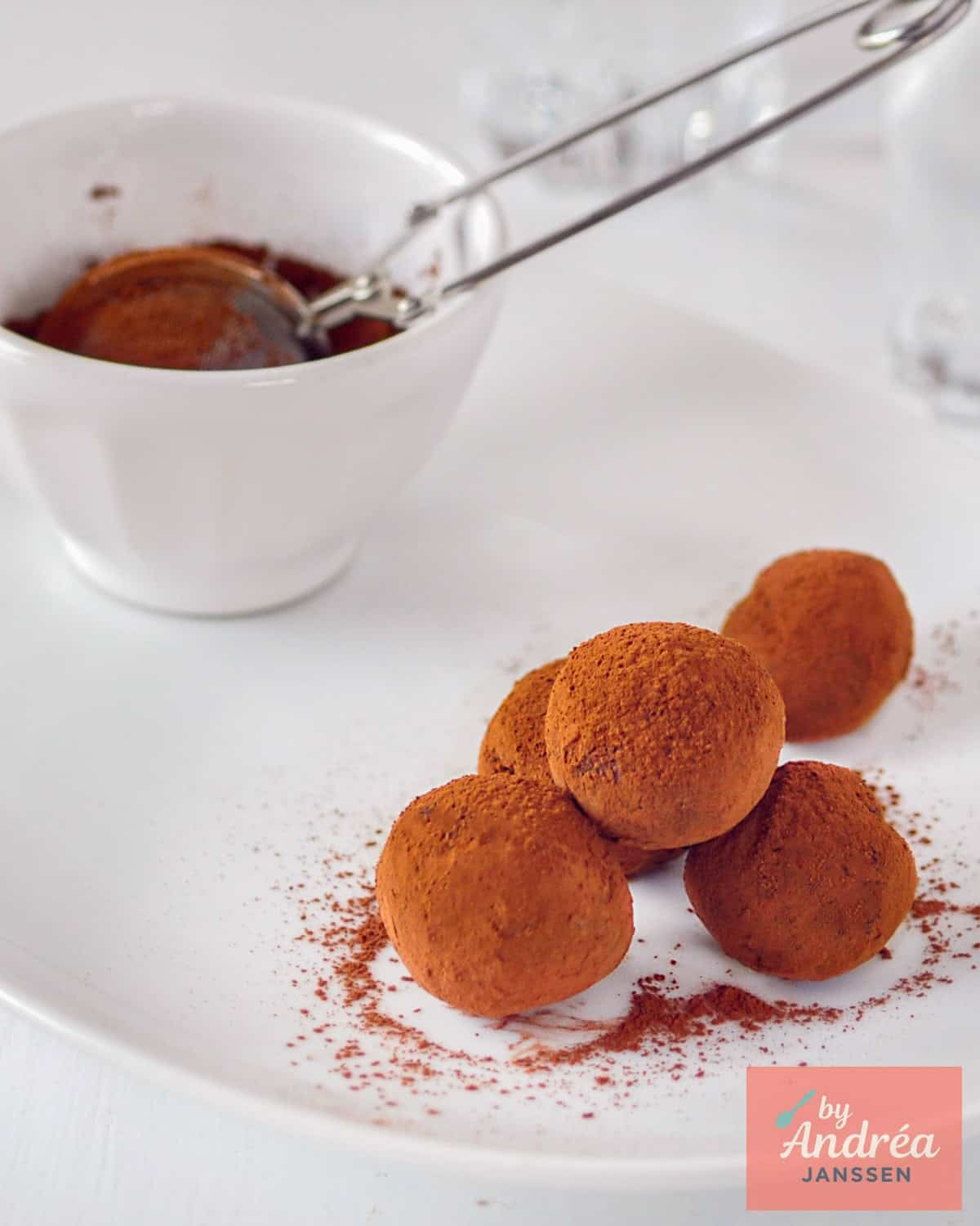 A small dish with five orange chocolate truffles. In the background, a small bowl of cocoa and a sieve.