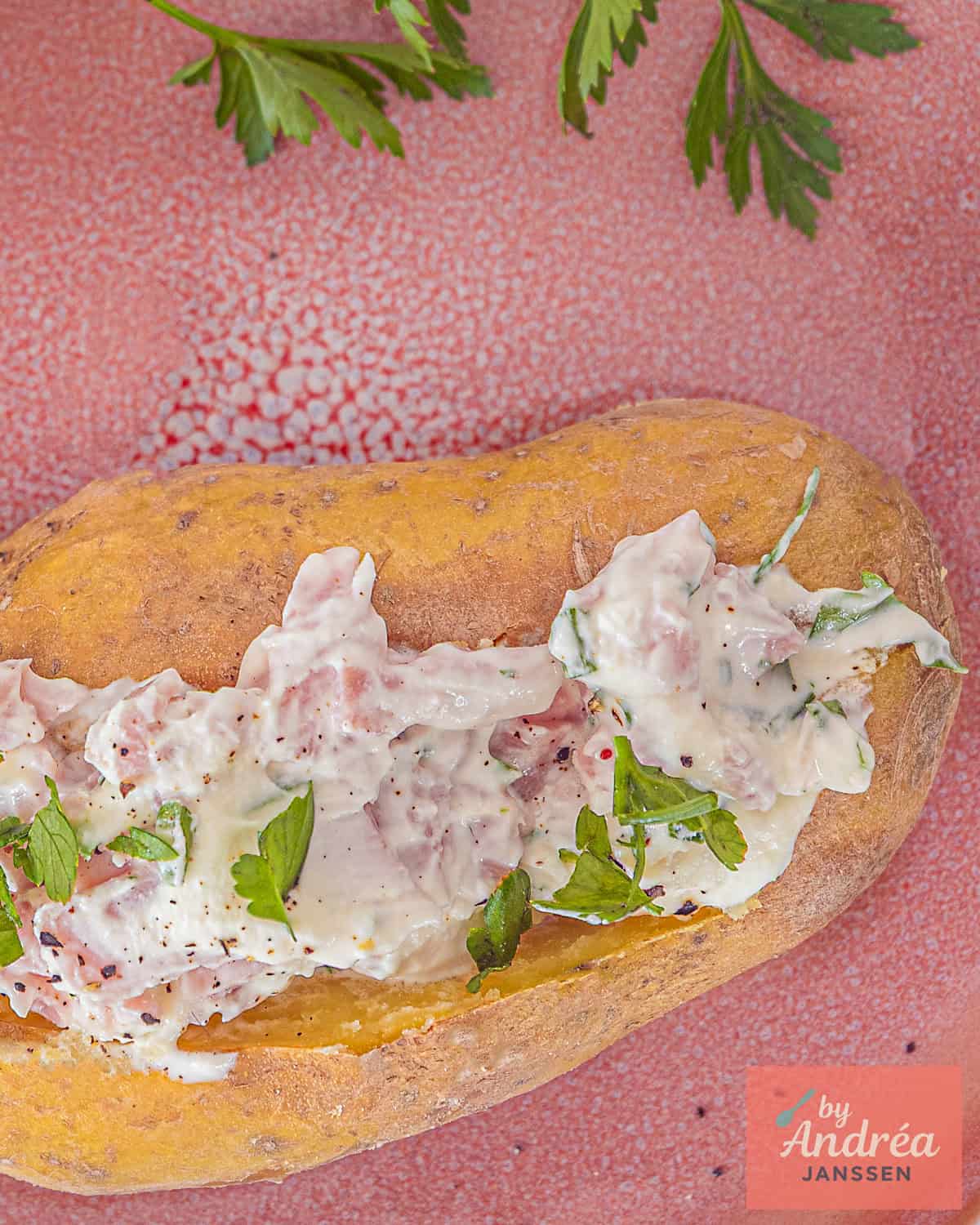 Een foto van bovenaf van een gebakken aardappel gevuld met kwark en ham