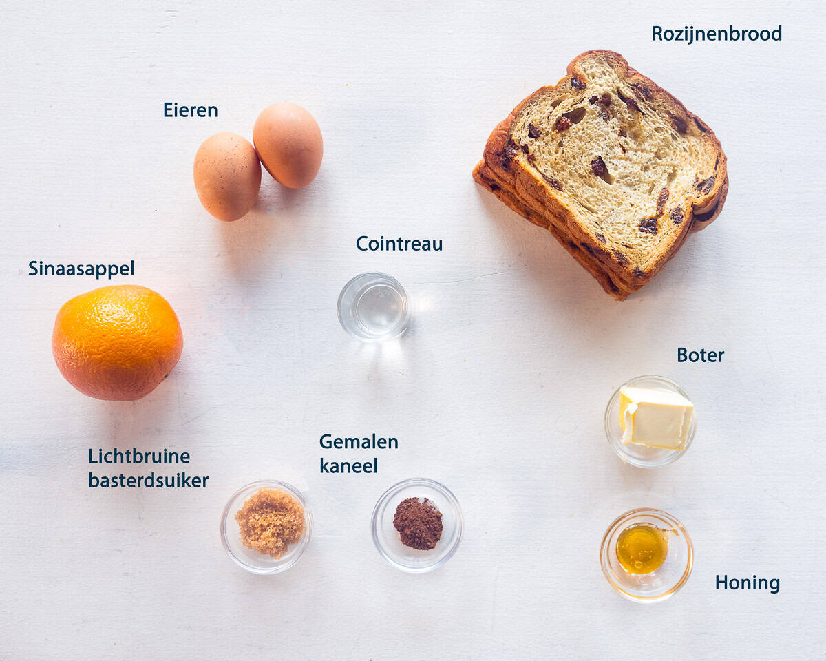 Ingredienten Luxe wentelteefjes met rozijnenbrood en sinaasappel op een witte ondergrond met tekst beschrijving.