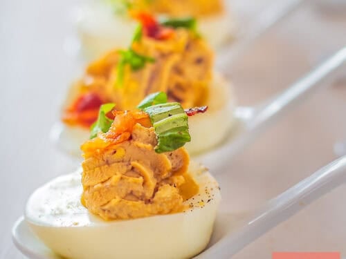 A square photo with a vertical row of Italian deviled eggs with balsamic and pancetta