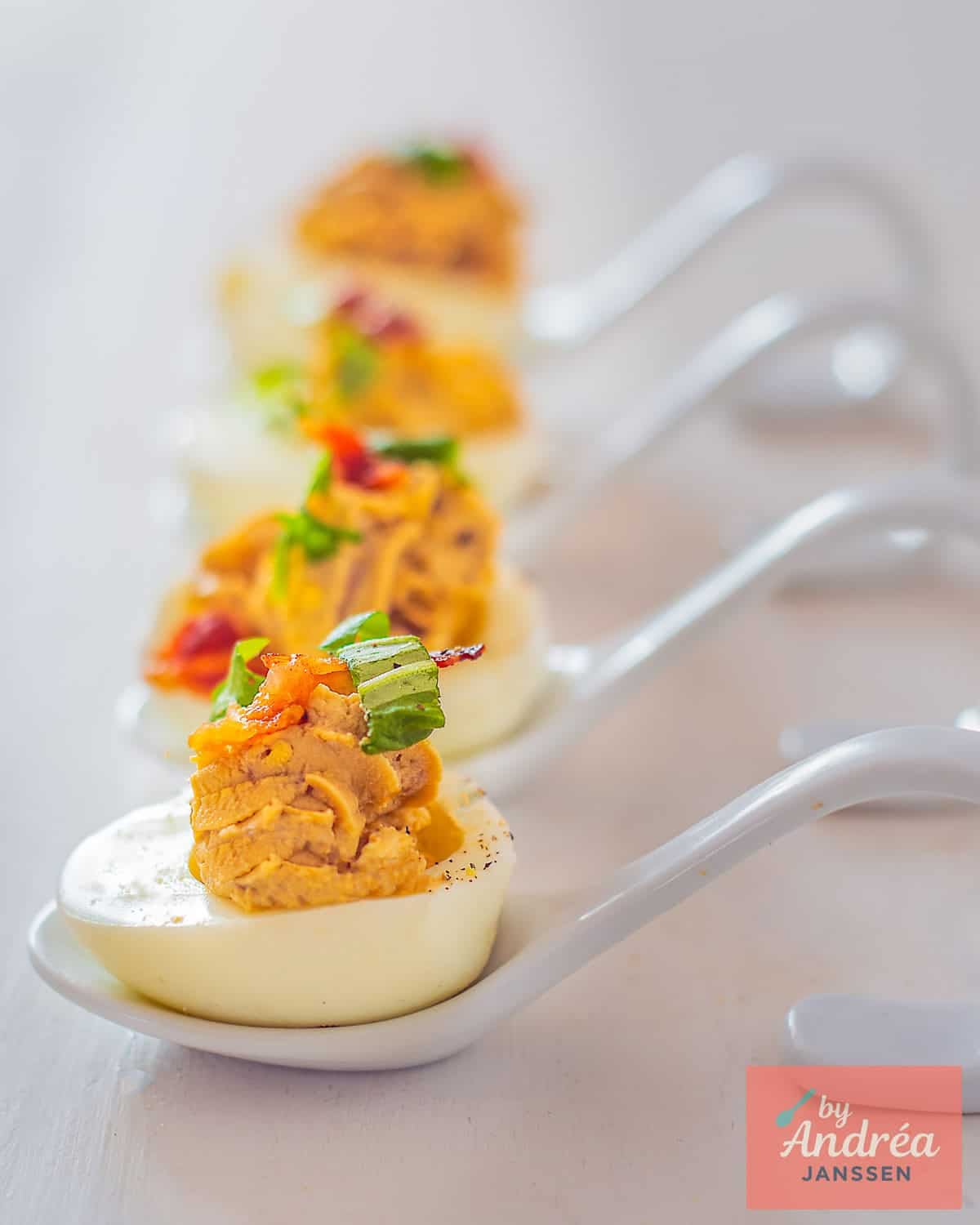 A row of four amuse spoons in a row with an Italian deviled egg with balsamic and Pancetta