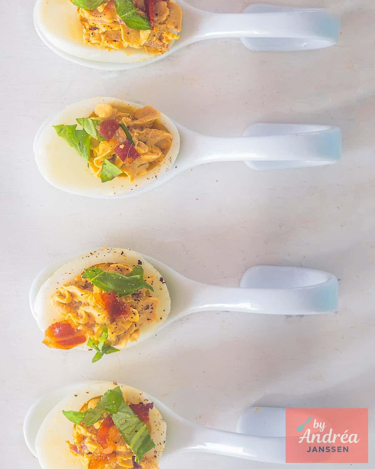 A photo from above of four white amuse-bouche spoons with a deviled egg with Pancetta and balsamic cream