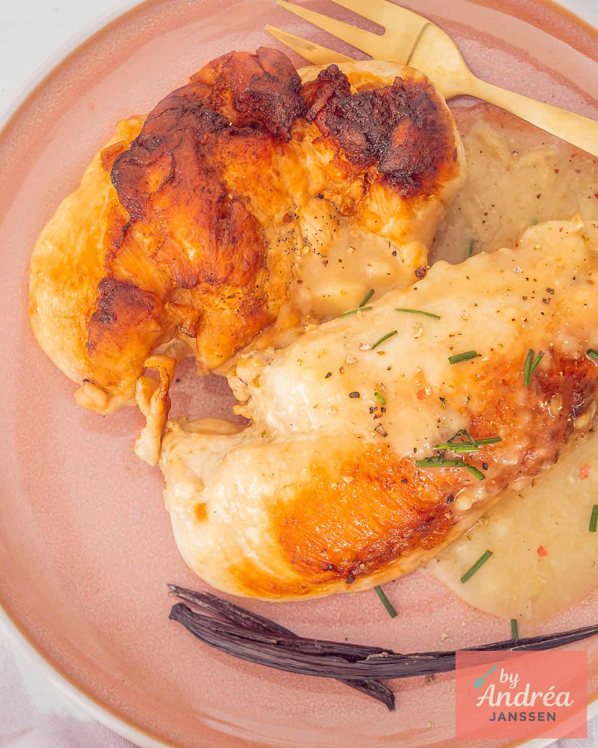 A photo from above of a pink plate with two fried chicken fillets with vanilla sauce and chives.