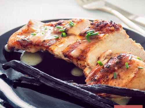 A square photo with chicken breast fried with vanilla sauce on a black plate.