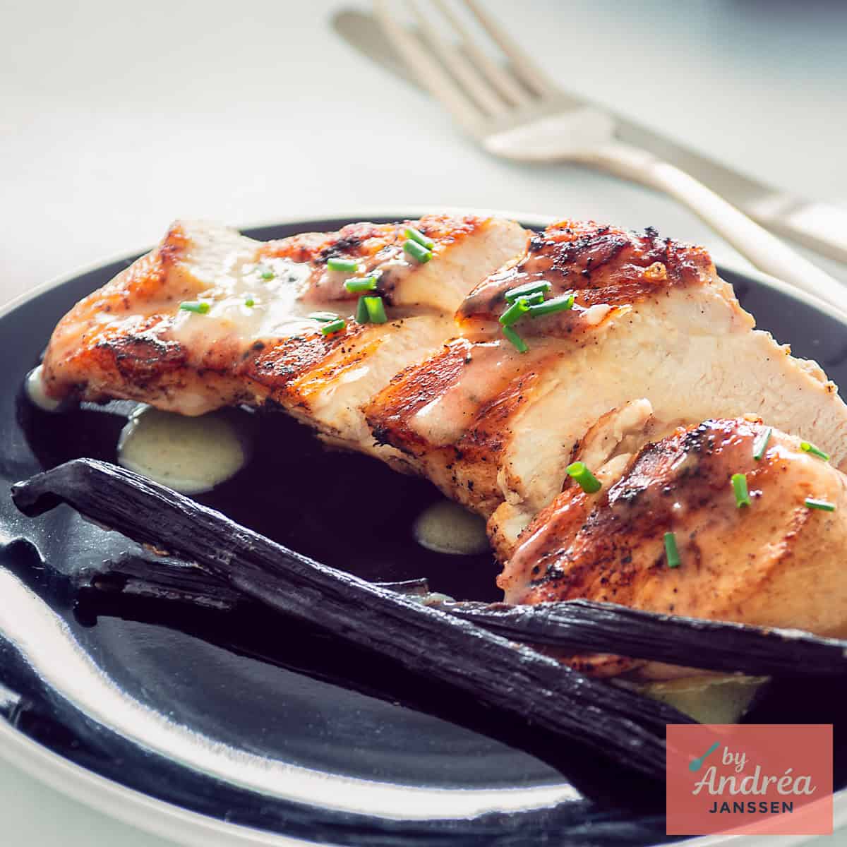 A square photo with chicken breast fried with vanilla sauce on a black plate.