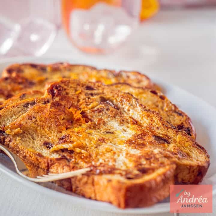 A square photo of a plate with three French toast slices with orange stacked on top of each other.