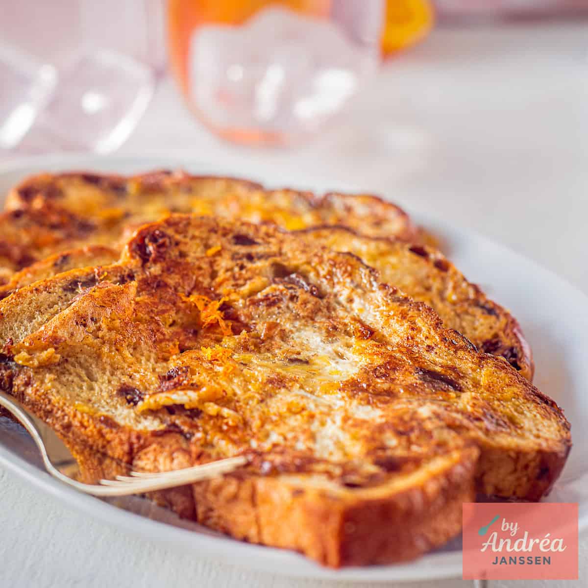A square photo of a plate with three French toast slices with orange stacked on top of each other.