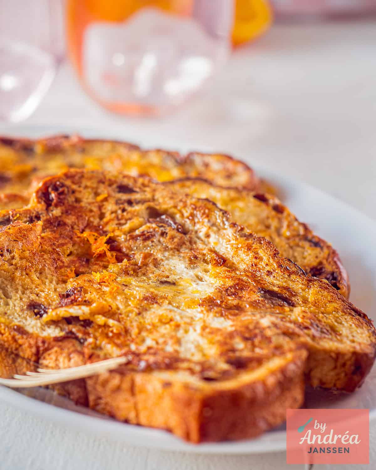 Een schaal met drie wentelteefjes met rozijnenbrood en sinaasappel.