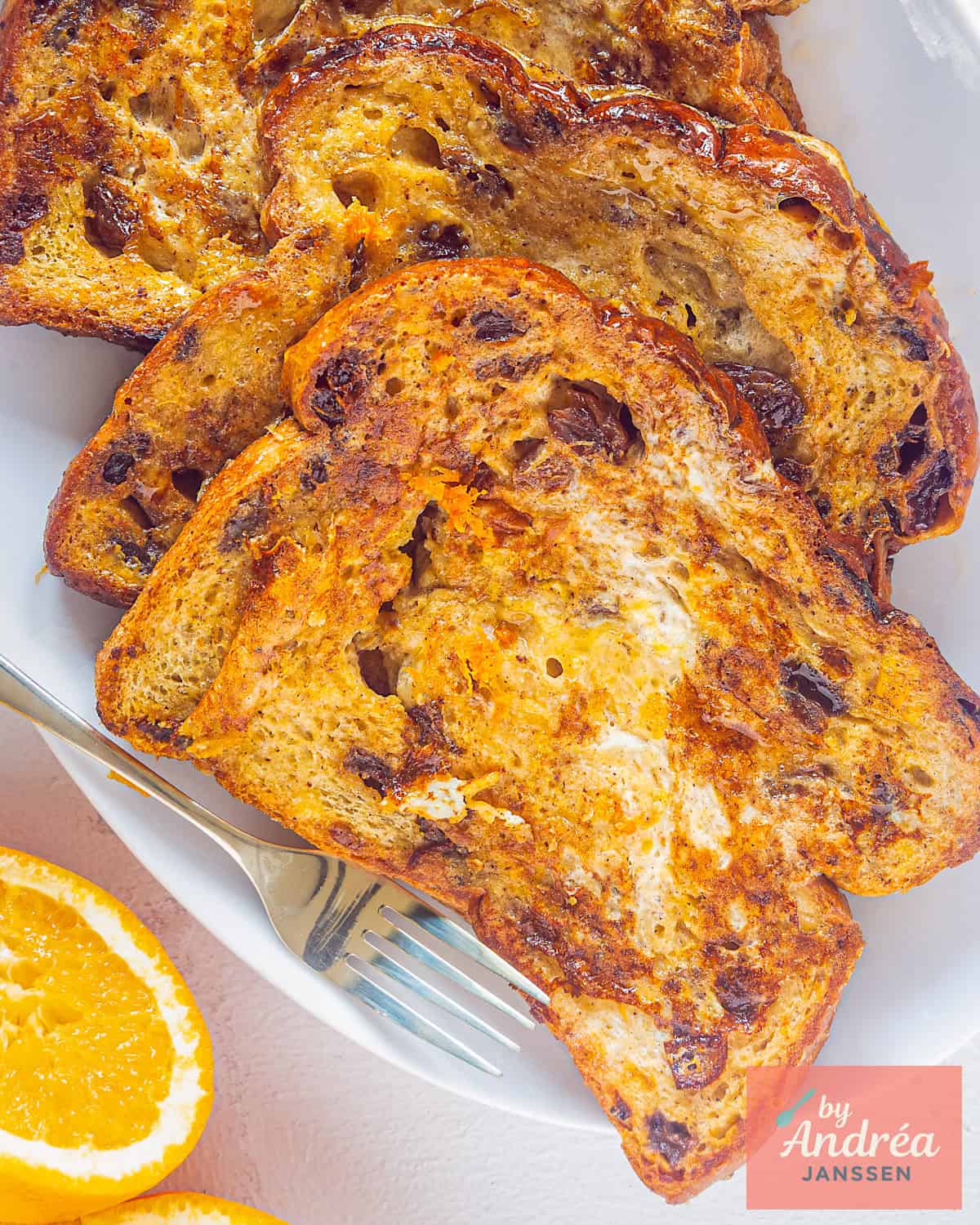Een foto van bovenaf van drie rozijnenbrood sneetjes omgetoverd tot luxe wentelteefjes met sinaasappel
