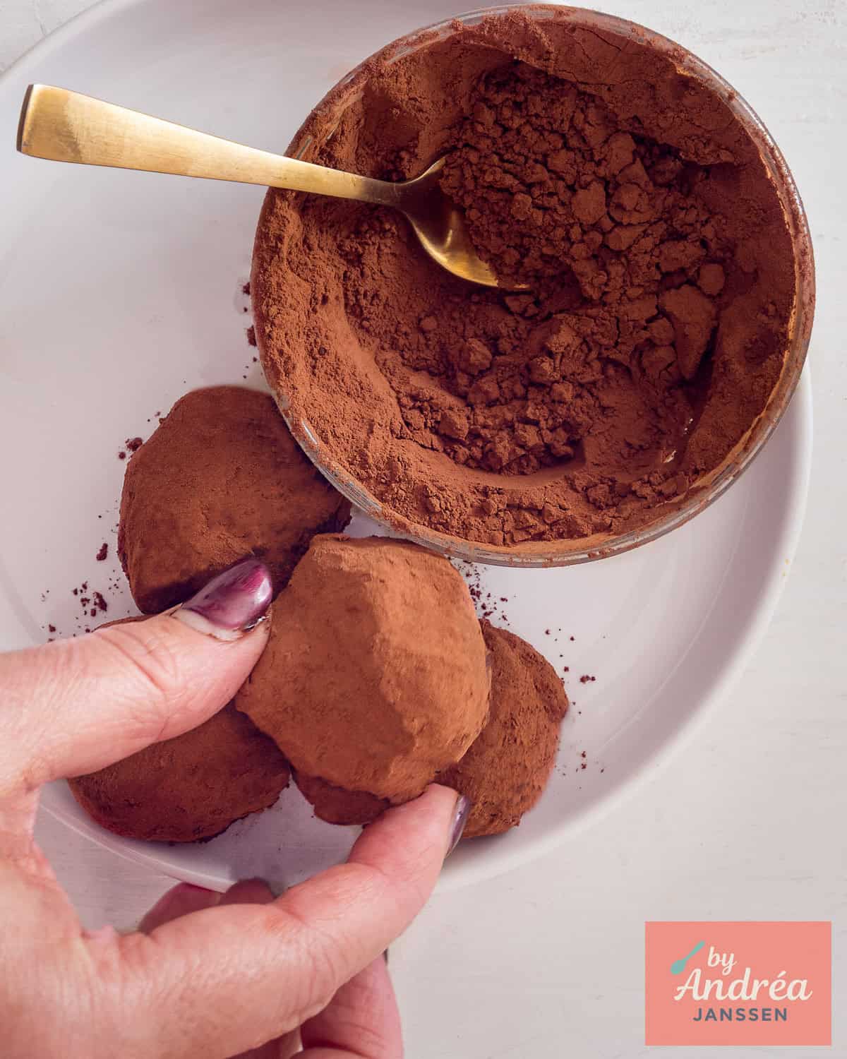 A hand taking an orange chocolate truffle from the plate.