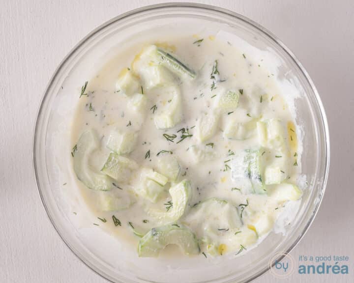 A bowl filled with yogurt marinade, cucumber and dill.