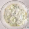 A bowl filled with yogurt marinade, cucumber and dill.