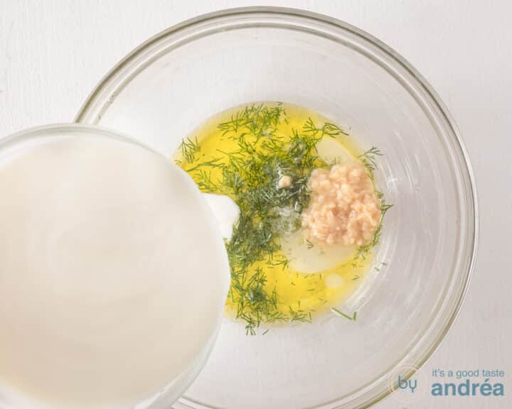 A glass bowl with olive oil, salt, dill and garlic. Greek yogurt is added.