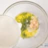 A glass bowl with olive oil, salt, dill and garlic. Greek yogurt is added.