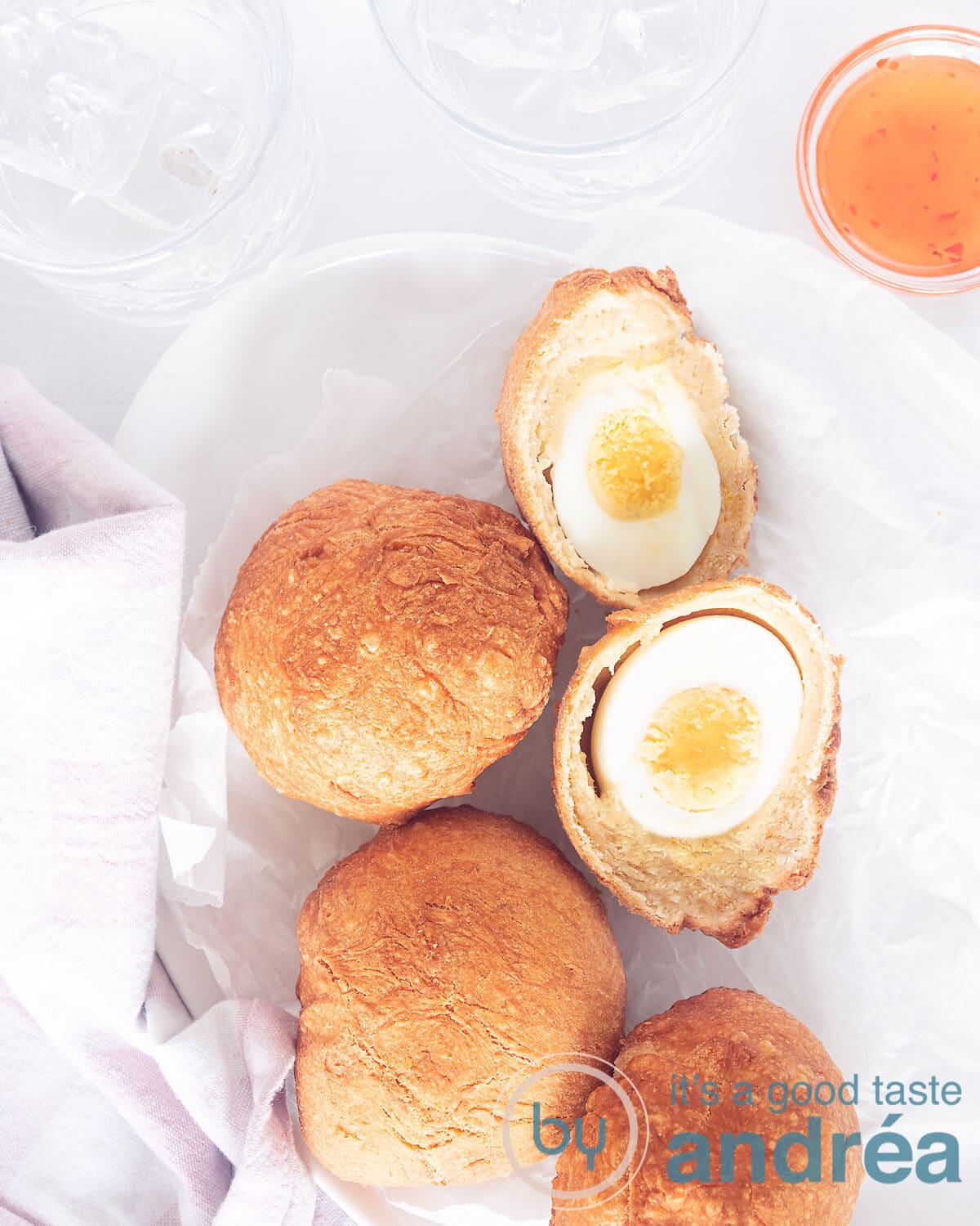 Een foto van bovenaf met een witte schaal met daarop Afrikaanse snacks met ei, één doormiddeen gesneden. Rechts bovenin een schaaltje met saus. Een witte ondergrond