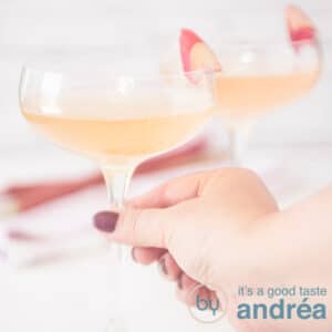 A square photo with two glasses filled with champagne and rhubarb syrup. A hand takes the glass