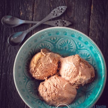 two silver spoons, a blue bowl with three scoops of chocolate ice cream