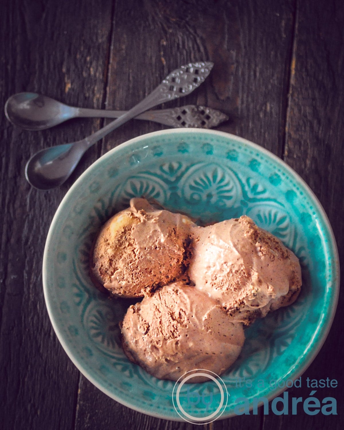 Een blauw schaaltje met drie bollen chocolade ijs op een zwarte ondergrond