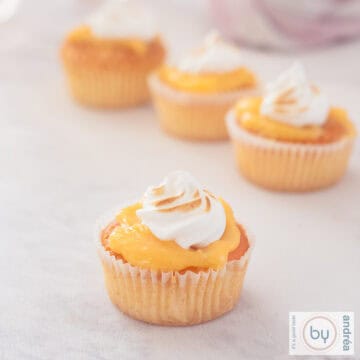 A square picture with four lemon and meringue cupcakes on a white marble background