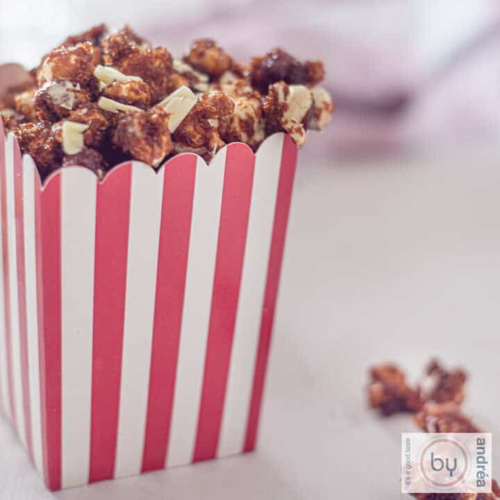 A square photo with a red and white striped container filled to the brim with caramel popcorn with white chocolate