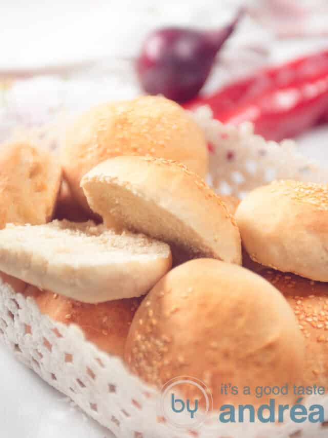 hamburger buns in a plastic basket on a white background. Some fresh vegetables in the background