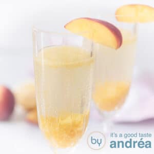 A square photo with two champagne glasses filled with Bellini cocktail. Peaches in the background