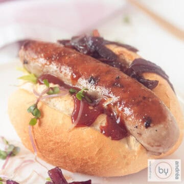 A square photo with a sandwich filled with grilled sausage and sweet caramelized onions
