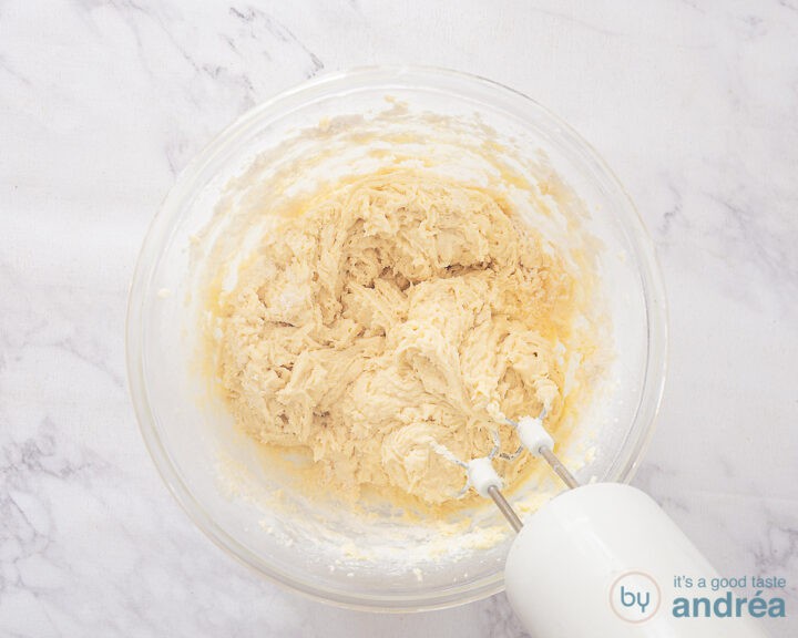 A glass bowl with cupcake batter and a mixer.