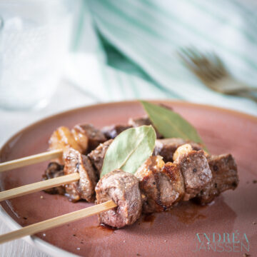 three Portuguese entrecote skewers on a pink plate with bay leaves