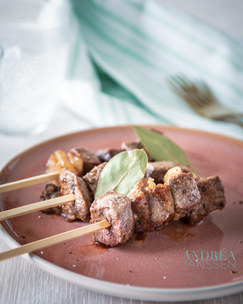 three Portuguese entrecote skewers on a pink plate with bay leaves