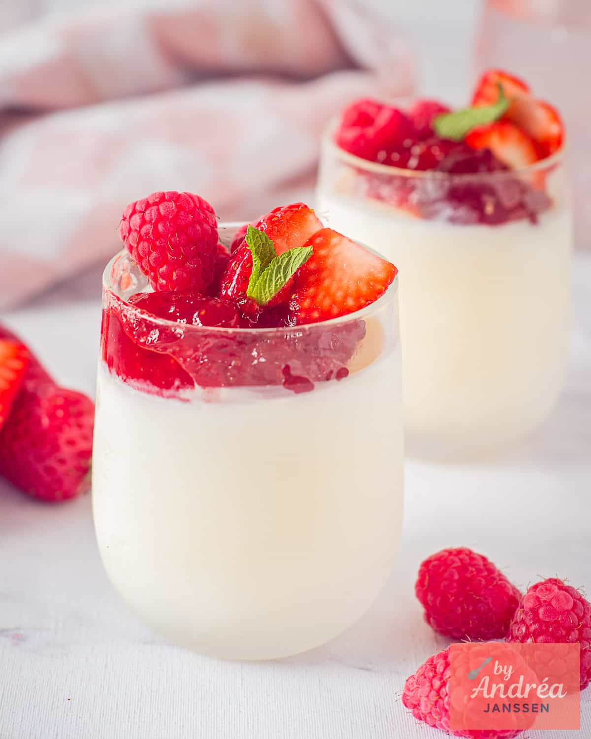 Two small glasses placed diagonally behind each other, with frozen yogurt at the bottom and a topping of jam and red fruit.