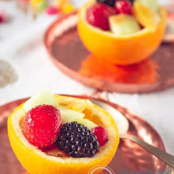 two orange bowls filled with fresh fruit on copper plates