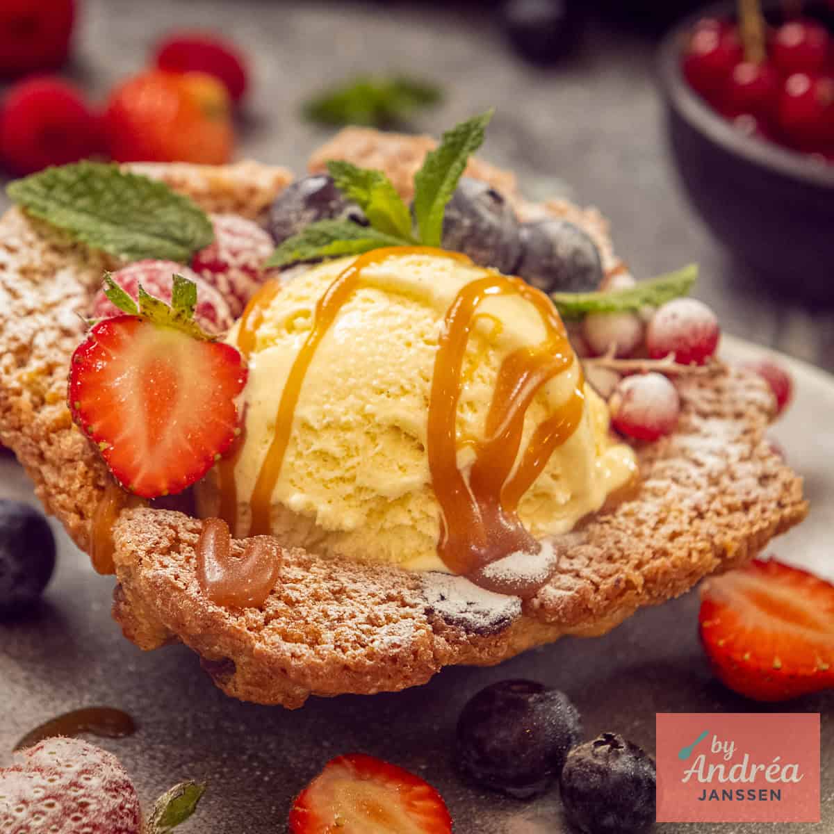 A square photo with a cookie cup containing vanilla ice cream with caramel sauce and fruit.